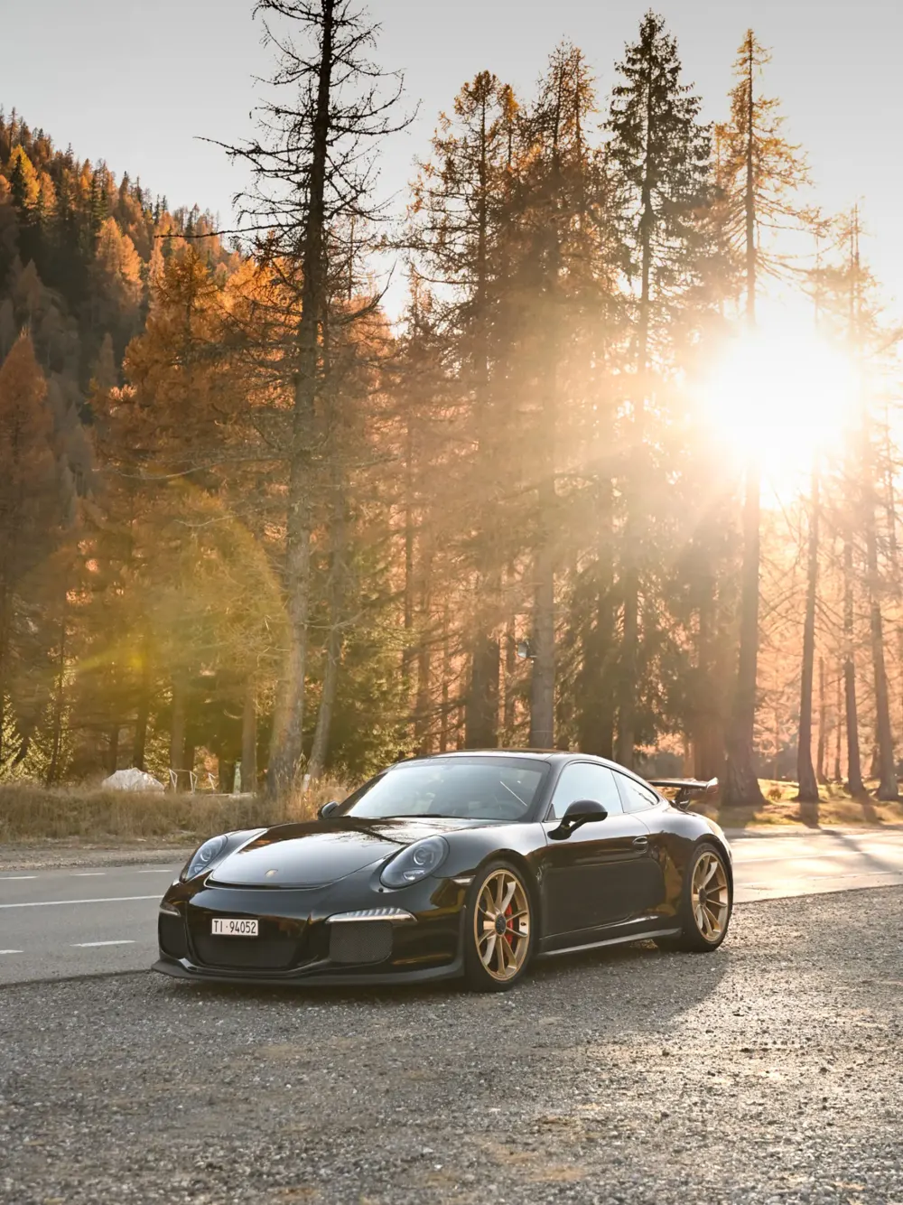 Una Porsche nera su una strada nel bosco al tramonto